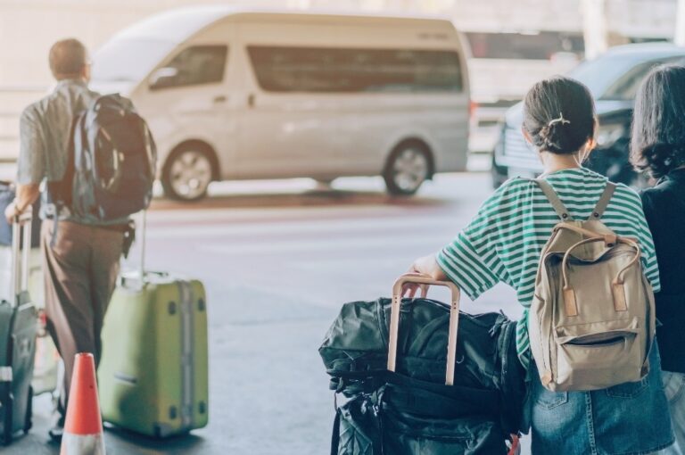 Passagiere mit großem Rollgepäck warten stehend auf ihr Auto am Ankunftsterminal des Flughafens.