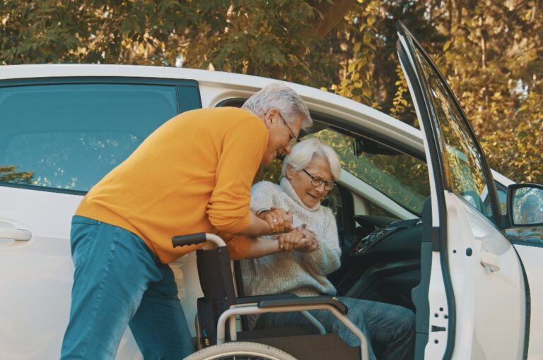 Mann hilft Frau beim Aussteigen aus dem Auto zum Rollstuhl.