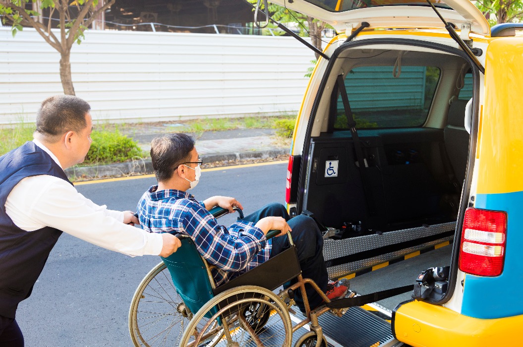 Fahrer hilft Mann im Rollstuhl beim Einsteigen ins Taxi
