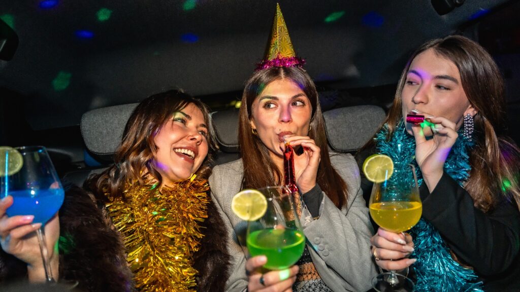 junge Frauen, die im Auto mit Cocktails und Partytröten feiern