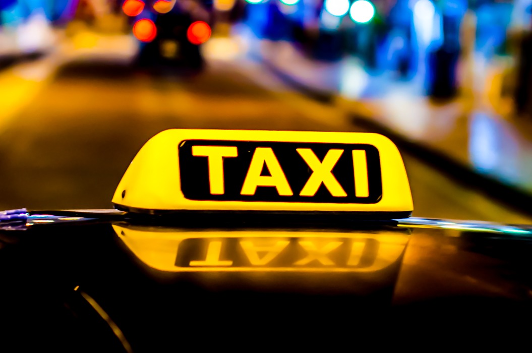 Nachtfoto eines Taxis. Das Taxischild auf dem Dach des Fahrzeugs leuchtet im Dunkeln.
